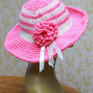 May include: A pink and white striped crochet sun hat with a pink crocheted flower and white lace trim.