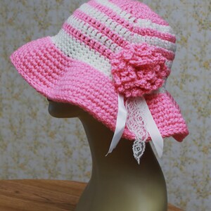 May include: A pink and white striped crochet sun hat with a pink crocheted flower and a white lace trim.