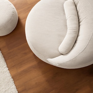 Puede incluir: Vista a&eacute;rea de dos muebles tapizados en pana color crema. Uno es un otom&aacute;n redondo, el otro una pieza m&aacute;s grande y redondeada con un coj&iacute;n curvo. Se encuentran sobre un suelo de madera junto a una alfombra blanca.