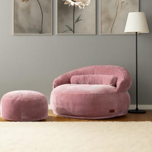 Puede incluir: Un sill&oacute;n de pana rosa con un otom&aacute;n a juego y una l&aacute;mpara de pie. Tres estampados florales enmarcados cuelgan de la pared gris sobre los muebles. La habitaci&oacute;n tiene una est&eacute;tica suave y acogedora.