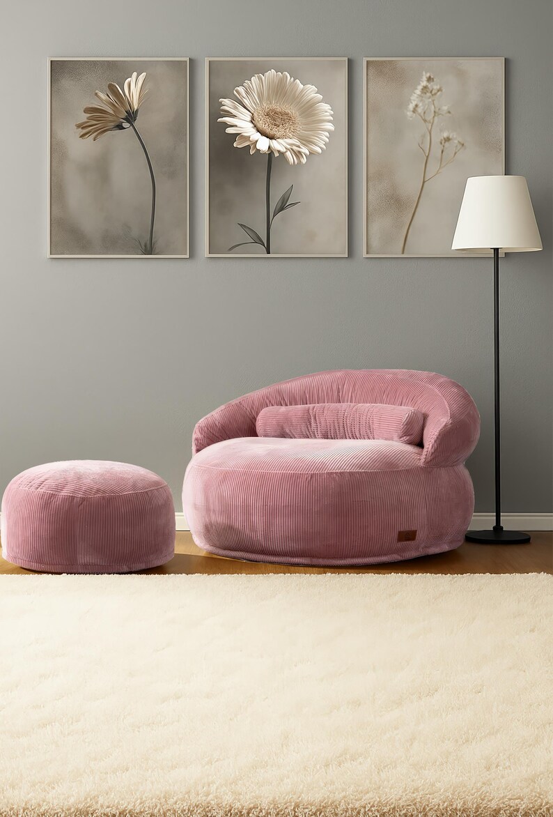 Puede incluir: Un sill&oacute;n de pana rosa con un otom&aacute;n a juego y una l&aacute;mpara de pie. Tres estampados florales enmarcados cuelgan de la pared gris sobre los muebles. La habitaci&oacute;n tiene una est&eacute;tica suave y acogedora.