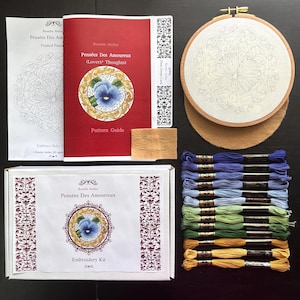 May include: An embroidery kit with a red and white box, a pattern guide, and an embroidery hoop. The kit includes embroidery floss in shades of blue, green, and yellow. The pattern guide is titled "Pensées Des Amoureux (Lovers' Thoughts)".