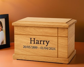 May include: A wooden urn with a rectangular shape and a light brown finish. The name "Harry" and dates 20/05/1889 - 01/04/2024 are printed on the front. The urn has a lid and sits on a base.