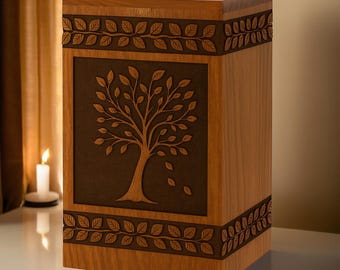 May include: A wooden urn with a tree design. The rectangular urn is made of light brown wood with a dark brown tree carved into the front panel. Leaf patterns border the top and bottom.