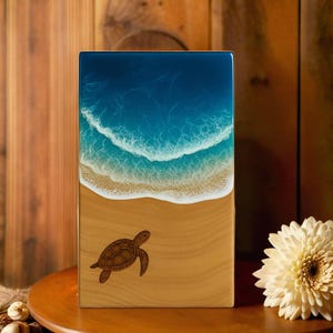 May include: A rectangular wooden plaque featuring a resin art ocean scene with white foamy waves crashing onto a sandy beach. A detailed brown sea turtle illustration is etched into the lower wooden section of the piece.