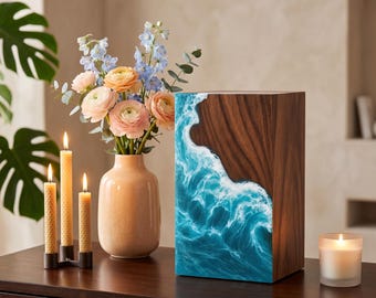 May include: A wooden decorative box with a wave design in shades of blue and white. The box is next to a vase of flowers, lit candles, and a lit candle in a glass holder. The flowers are pink, peach, and blue.