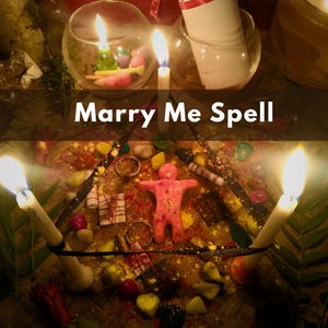 Op de afbeelding: De afbeelding toont een "Marry Me Spell" met brandende kaarsen, een roze figuur, ringen en kleurrijke stenen. Een rol en glazen kommen zijn ook aanwezig, op een geweven oppervlak.