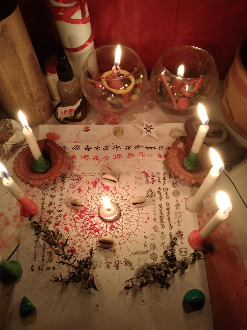 May include: A white paper sheet featuring intricate black geometric patterns, symbols, and text, surrounded by six lit white candles in clay holders, four cowrie shells, two glass bowls filled with colorful stones, and scattered red powder.