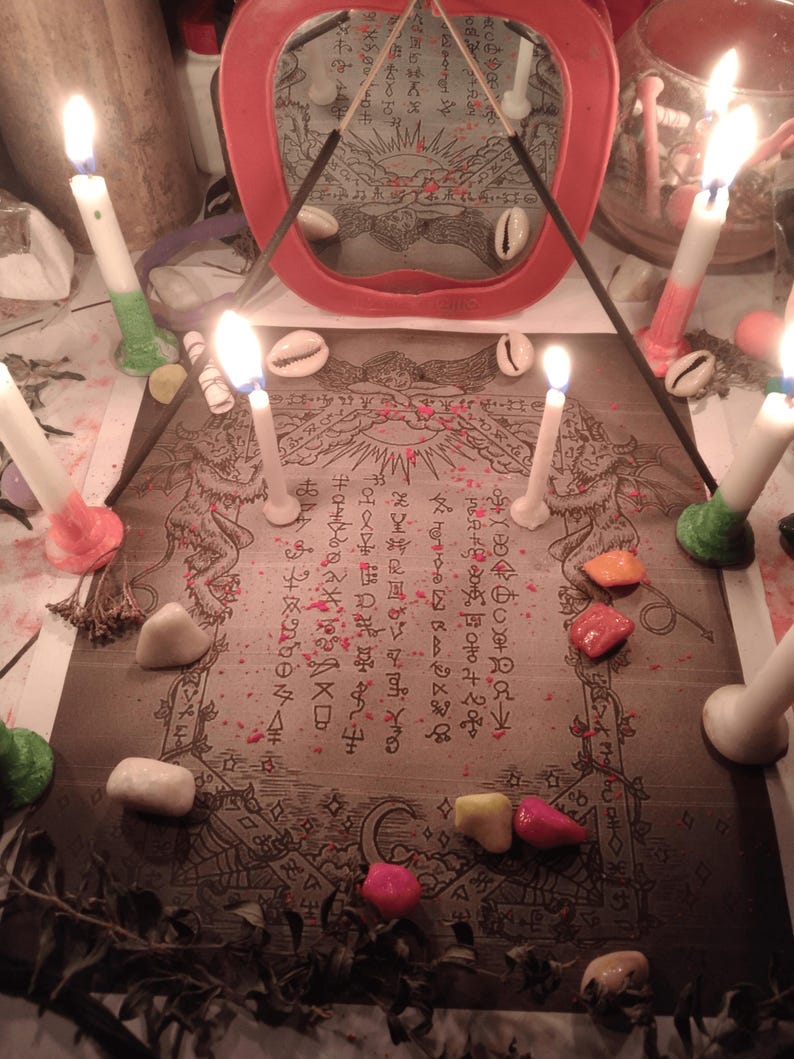 May include: A rectangular print featuring intricate line art of mythical creatures and occult symbols, surrounded by six lit white candles with colored bases, scattered cowrie shells, small colorful stones, and a red-framed mirror in the background.