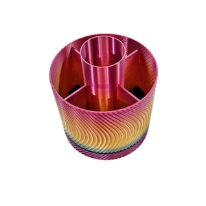 Könnte beinhalten: Ein mehrfarbiger Schreibtisch-Organizer mit einem zentralen zylindrischen Fach und mehreren umliegenden Abschnitten. Die Außenseite weist ein wellenartiges Muster in Rosa-, Gelb- und Blautönen auf. Der Innenraum ist einfarbig rosa.