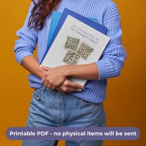 May include: A white booklet titled An Introduction to The Zentangle Method with three black and white patterned square illustrations on the cover, held in front of a blue folder against a solid yellow background. The text is clearly visible.