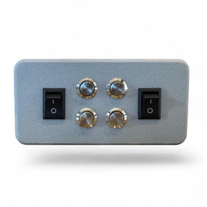 Puede incluir: Una caja de control rectangular gris con dos interruptores basculantes negros y cuatro botones plateados. Los interruptores est&aacute;n situados a la izquierda y a la derecha, mientras que los botones est&aacute;n en el centro.