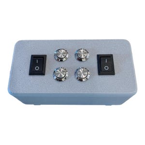 Puede incluir: Una caja de control rectangular gris claro con dos interruptores basculantes de encendido/apagado negros y cuatro interruptores de bot&oacute;n plateados. La caja tiene una superficie texturizada, dise&ntilde;ada para aplicaciones de control el&eacute;ctrico.