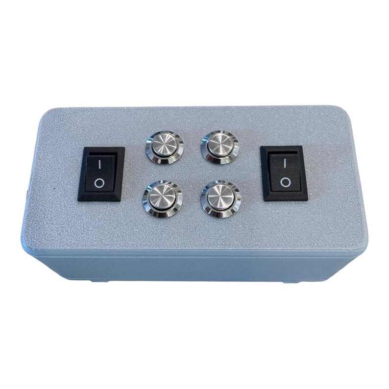 Puede incluir: Una caja de control rectangular gris claro con dos interruptores basculantes de encendido/apagado negros y cuatro interruptores de bot&oacute;n plateados. La caja tiene una superficie texturizada, dise&ntilde;ada para aplicaciones de control el&eacute;ctrico.