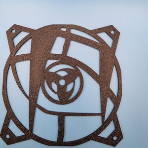 Op de afbeelding: Een vierkant metalen ventilatorrooster in bronskleur met een getextureerde, gehamerde afwerking. Het ontwerp bevat een cirkelvormig frame met vier montagegaten in de hoeken en een gestileerd centraal embleem met drie gebogen bladen.