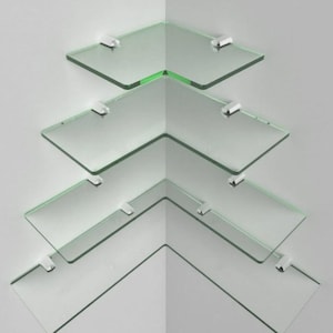 Peut inclure: Ensemble de quatre étagères d'angle en verre transparent, chacune soutenue par deux supports argentés. Les étagères sont disposées en quinconce sur un mur blanc, créant une esthétique moderne et minimaliste.