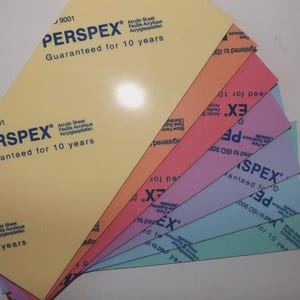 Puede incluir: Un abanico de láminas acrílicas Perspex de colores, incluyendo amarillo, naranja, rosa, morado y azul. Cada lámina está etiquetada con el nombre de la marca y el texto "Guaranteed for 10 years."