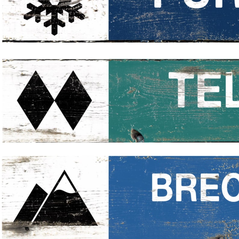 May include: A collage of wooden signs with a distressed finish. The signs feature white text and black graphic elements, including a snowflake, two black diamonds, and mountain silhouettes. The signs are painted in blue, green, and white.
