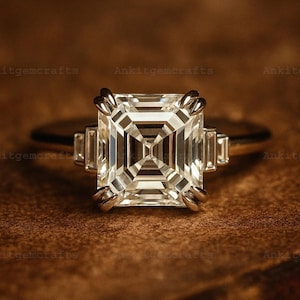 May include: A close-up of a diamond ring with a large, square-cut center stone and smaller rectangular side stones. The ring is set on a thin, gold band. The background is a warm, brown tone. The text "Ankitgemcrafts" is repeated.