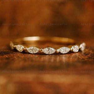 May include: A gold band ring with alternating round and marquise-cut clear gemstones. The ring is set on a brown surface. The ring is a delicate piece of jewelry.