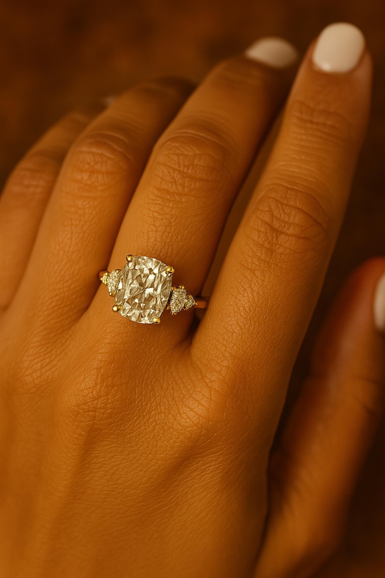May include: A gold ring featuring a large, cushion-cut diamond as the centerpiece, flanked by smaller, pear-shaped diamonds on each side. The ring is set on a gold band, showcasing a classic and elegant design.