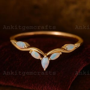 May include: A gold-colored ring with a curved design, featuring five oval-shaped opalescent gemstones. The ring is set against a dark red background, with the text "Ankitgemcrafts" visible.