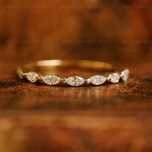 May include: A gold band ring with a series of marquise-cut and round-cut diamonds. The ring is set on a brown surface. The ring is a piece of jewelry.