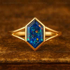 May include: A gold ring with a hexagonal, dark blue opal gemstone. The opal has flecks of green, red, and yellow. The ring's band has a split design on each side of the gemstone.