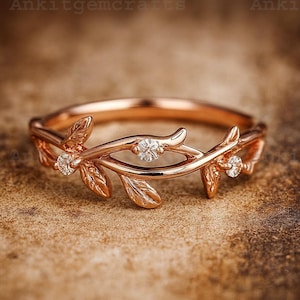 Op de afbeelding: Roségouden ring met een delicaat blad- en wijnstokontwerp. De ring is versierd met drie kleine, sprankelende diamanten. De band heeft een gladde, gepolijste afwerking. Een door de natuur geïnspireerd sieraad.