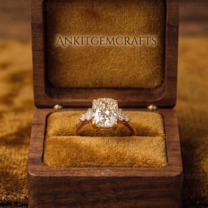 May include: A gold ring with a large, rectangular, clear gemstone, flanked by smaller stones, set in a wooden box with the text "ANKITGMCRAFTS". The box has a velvet interior.