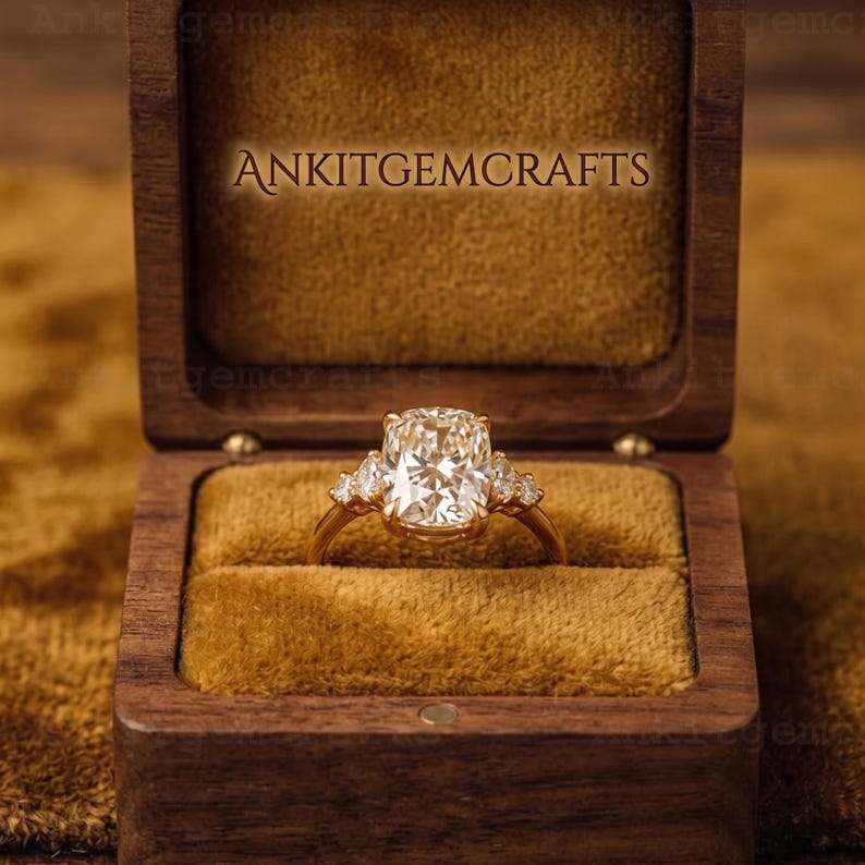 May include: A gold ring with a large, rectangular, clear gemstone, flanked by smaller stones, set in a wooden box with the text "ANKITGMCRAFTS". The box has a velvet interior.
