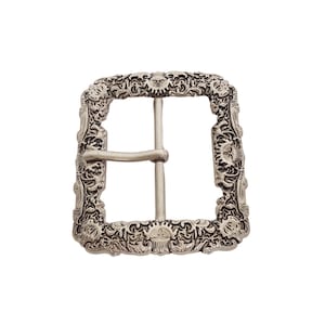 May include: A silver-colored, square belt buckle with an ornate, floral design around the edges. The buckle has a central bar and a tongue for securing a belt. The decorative border features detailed scrollwork and sun-like motifs.