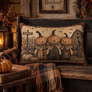 May include: A rectangular throw pillow featuring a printed illustration of three pumpkin-headed figures standing in a cornfield. The scene includes a wooden fence, a barn, a full moon, and bats against a dark sky. The pillow has a decorative border.