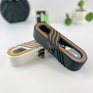 May include: Two wooden jewelry boxes. One is black with a clear top and a decorative wood grain design. The other is white with a similar wood grain design. Both have a clasp closure.