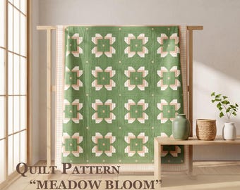 May include: A quilt featuring a repeating geometric floral pattern in sage green, cream, and soft pink. The text reads: Quilt Pattern "MEADOW BLOOM" Quilt Sizes: 67" x 67"/85" x 85"/103" x 103". The quilt is displayed on a wooden frame.