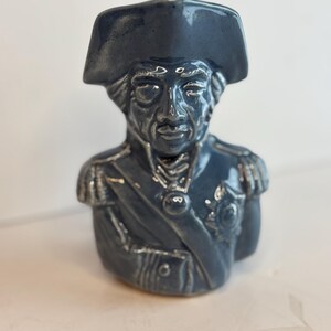 May include: A ceramic bust of a historical figure, featuring a dark blue glaze. The figure wears a tricorn hat and a military uniform with epaulettes and a sash. The bust is a decorative item.