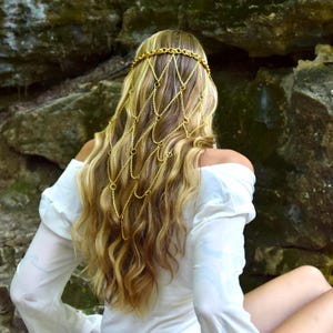 May include: A gold-toned metal chain headpiece featuring a delicate, interconnected net design that drapes over the back of the head. The accessory is constructed from thin, polished links and small circular rings, creating a cascading, layered effect.