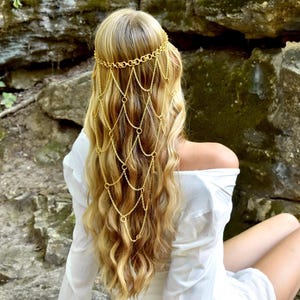 May include: A gold-toned hair accessory featuring a delicate chain headpiece that drapes over the back of the head. The design consists of a circular link headband connected to a cascading net of fine gold chains that hang down the hair.