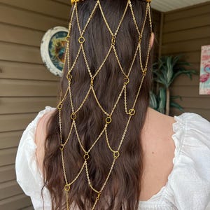 May include: A gold-toned metal headpiece featuring a horizontal band of interlocking rings that sits across the crown of the head, with a cascading net-like veil of delicate gold chains and small circular rings draping down the back of the hair.