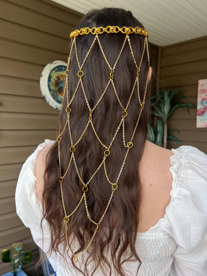 May include: A gold-toned metal headpiece featuring a horizontal band of interlocking rings that sits across the crown of the head, with a cascading net-like veil of delicate gold chains and small circular rings draping down the back of the hair.