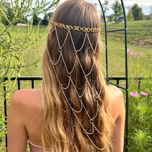 May include: A gold-toned headpiece featuring a horizontal band of interlocking circular links. Multiple delicate gold chains drape downward from the band, connected by small circular rings, creating a layered, cascading net-like effect.