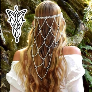 K&ouml;nnte beinhalten: Ein silberfarbener Ketten-Kopfschmuck mit einem zarten, drapierten Netzdesign, das den Hinterkopf hinunterf&auml;llt. Das Accessoire besteht aus miteinander verbundenen Metallringen und feinen Ketten, die ein geschichtetes, netzartiges Aussehen erzeugen.