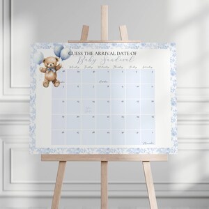 May include: A baby arrival date guessing game displayed on a wooden easel. The calendar features a watercolor teddy bear holding blue balloons. The text reads "Guess the Arrival Date of Baby [Name]" with a floral border.