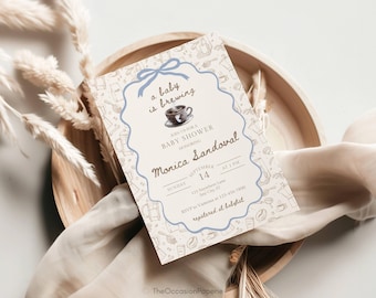 Puede incluir: Una tarjeta de invitación rectangular para baby shower con un borde festoneado azul claro y un lazo en la parte superior. El texto dice a baby is brewing, baby shower, honoring Monica Sandoval, Sunday September 14 at 2 PM y detalles de RSVP.