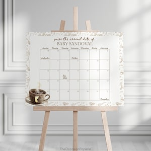 May include: A white calendar on a wooden easel with the text "guess the arrival date of BABY SANDOVAL". The calendar has dates for September, October, and November. A coffee cup with a footprint is on the bottom left.