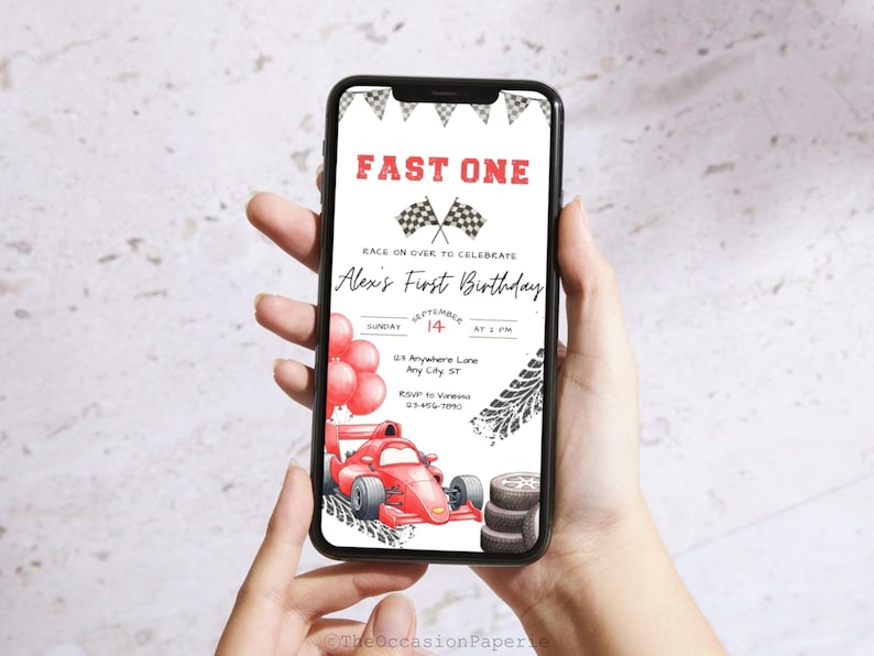 May include: A smartphone displays a red and white race car themed birthday invitation. The invitation reads "Fast One" and includes a race car illustration, balloons, and the text "Alex's First Birthday".