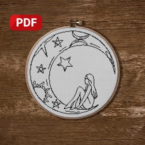 Può includere: Un motivo a punto croce in bianco e nero in un telaio da ricamo in legno. Il disegno presenta una luna crescente con stelle e una figura seduta. L'icona PDF si trova in alto a sinistra.
