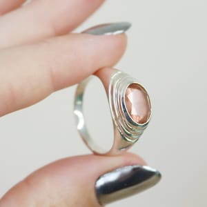 May include: A silver ring with a pink oval gemstone set in a textured band.