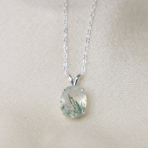 Op de afbeelding: Een zilveren ketting met een groene en witte agaat hanger. De hanger is ovaalvormig en heeft een delicate zilveren rand.