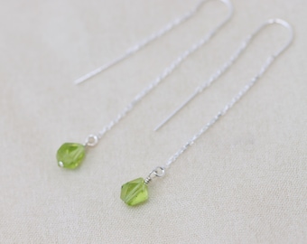 May include: A pair of silver chain earrings with green gemstone drops. The earrings are delicate and dangle from the earlobe.
